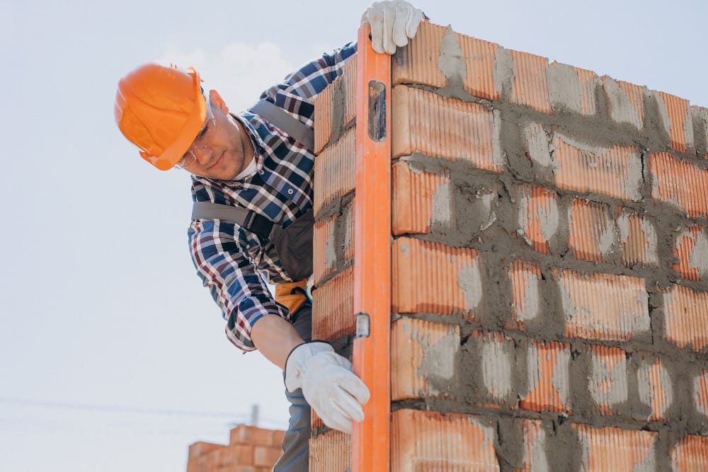 Trabajador construyendo una pared de ladrillos, nivelando con un producto de un grupo de compras.